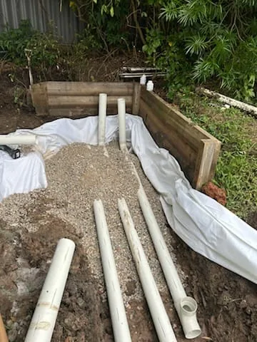 Slotted drainage pipes laid on gravel behind a timber retaining wall