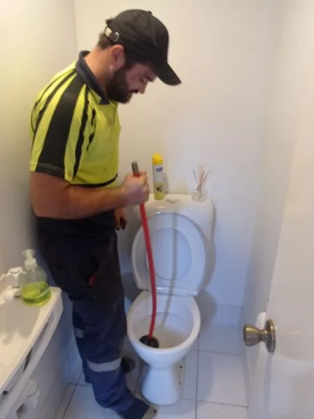 Plumber clearing a blocked toilet with a drain snake