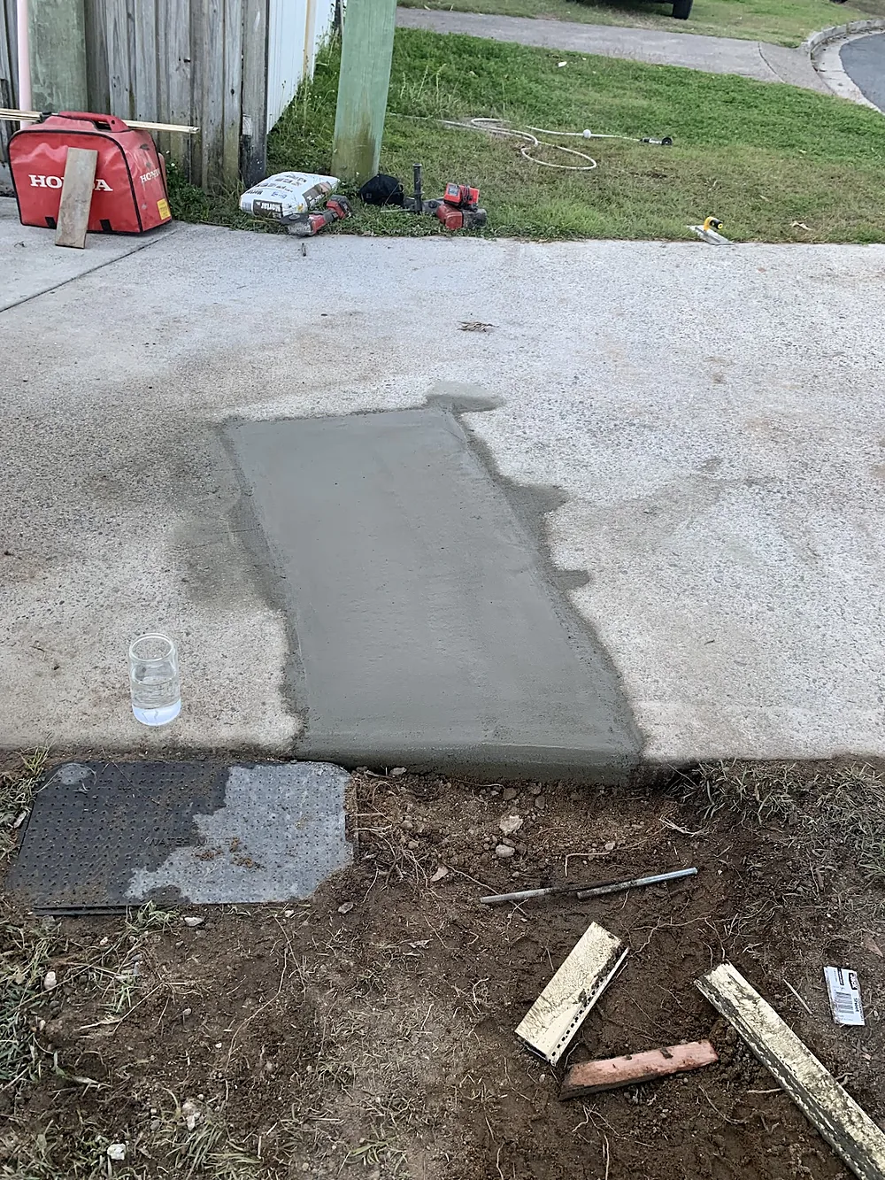 Driveway patched with fresh concrete after a drain repair, pit lid beside it