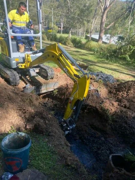 Yellow mini excavator digging a wet trench in a backyard