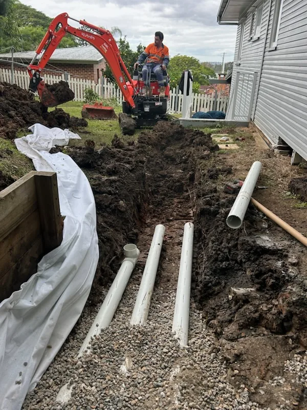 Mini excavator beside a new trench with slotted drainage pipes on gravel and geotextile fabric