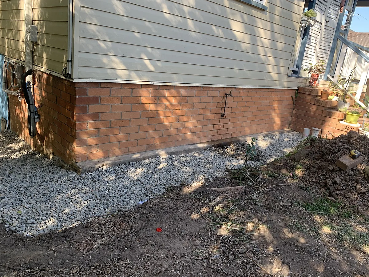 Fresh gravel drainage run along the brick base of a house