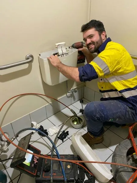 Linken in hi-vis repairing a toilet cistern, with a drain camera unit on the floor