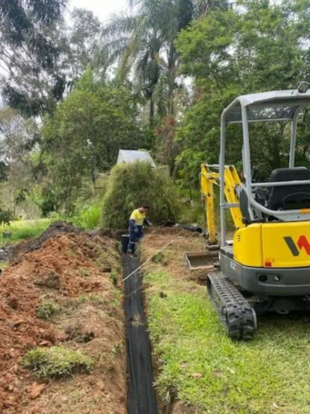 Long narrow trench cut across a lawn beside a mini excavator